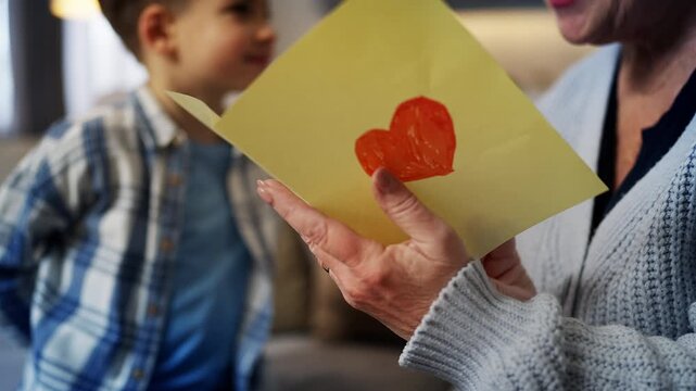 Adorable little boy giving handcrafted birthday card to grandma, family moment