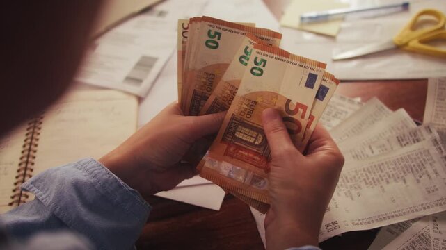 Close up of hands counting euros while sitting at a table. Utility bills and receipts are on the table. The process of calculating a family budget. High quality 4k footage