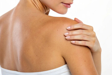 Fototapeta premium A close-up of a woman's smooth, sun-kissed bare shoulder and upper back with her hand gently touching it against a white background.