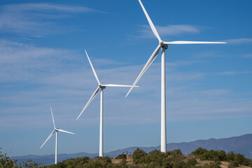 Fototapeta premium Three wind turbines rise from a hilly landscape under a clear sky, symbolizing clean energy and modern sustainability.