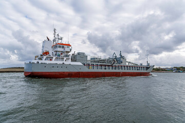 Fototapeta premium Cargo Ship Maneuvering Near Shoreline on Overcast Day
