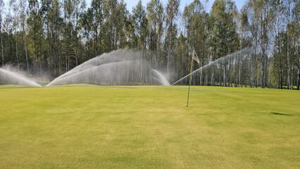 Golf course maintenance with sprinklers operating on a sunny day in a tranquil green landscape concept