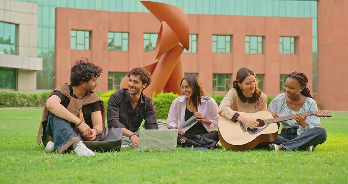 Indian young adult gen z female woman hold guitar play music man male group sing new song sitting garden park Happy relax girl boy team guy spend break time mood have fun joy enjoy new day place	