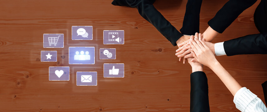 Diverse team members join hands on a wooden desk, symbolizing unity and collaboration while technology icons represent social networking and communication aspects. Trope