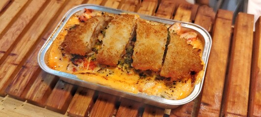 Crispy Chicken Katsu with Japanese Rice Mentai Sauce Served in a Alumunium Foil Container on Wood Table. Culinary Business Concept. Food Photography Presentation