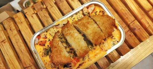 Crispy Chicken Katsu with Japanese Rice Mentai Sauce Served in a Alumunium Foil Container on Wood Table. Culinary Business Concept. Food Photography Presentation