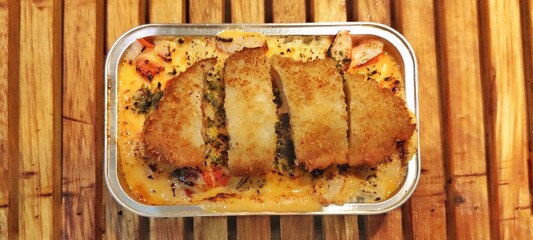 Crispy Chicken Katsu with Japanese Rice Mentai Sauce Served in a Alumunium Foil Container on Wood Table. Culinary Business Concept. Food Photography Presentation