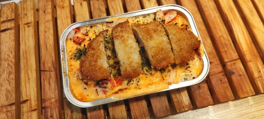 Crispy Chicken Katsu with Japanese Rice Mentai Sauce Served in a Alumunium Foil Container on Wood Table. Culinary Business Concept. Food Photography Presentation