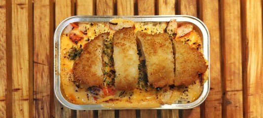 Crispy Chicken Katsu with Japanese Rice Mentai Sauce Served in a Alumunium Foil Container on Wood Table. Culinary Business Concept. Food Photography Presentation