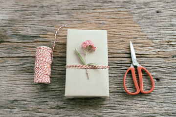 Gift box wrapped in paper kraft and small flower arranged on table with rope and scissors