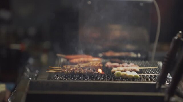 Slow motion showing meat grilling over open flames at a yatai barbecue in Fukuoka, Japan, with glowing embers, smoke, and warm tones highlighting street food energy