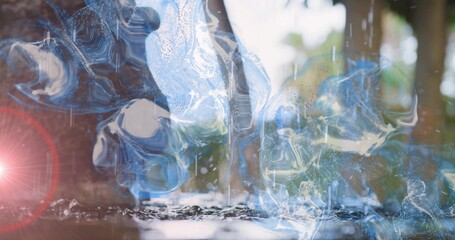 Floating glassy blue water swirls creating reflections on shallow pool near trees with lens flare