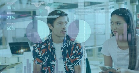 Coworkers discussing in office, man in printed shirt, woman in light tee holding tablet with charts