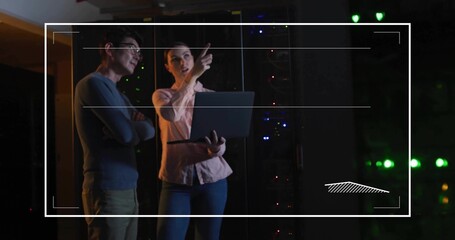 Pointing woman holding laptop and colleague watching server racks with LEDs and HUD in server room