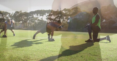 Training trio doing rows on sunny field, using weights, coach kneeling wearing green tank and shoes