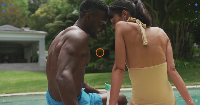 Sitting couple leaning at backyard pool, wearing blue trunks, yellow halter suit, drink umbrella