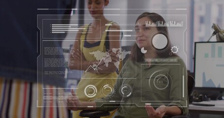 Seated woman in green shirt gesturing while reviewing data at open-plan office, with HUD overlay