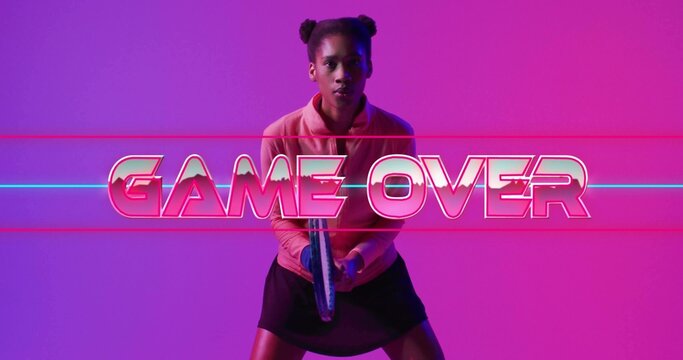 Standing woman in pink top and black skirt holding controller at studio, GAME OVER neon