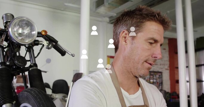 Standing mechanic wearing white T-shirt brown apron, adjusting motorcycle front end in workshop - Powered by Adobe
