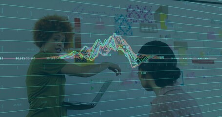 Pointing two women working at office wall with open laptop sticky notes, green top, printed blouse