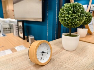 A stylish wooden alarm clock paired with a potted plant on a light wooden table, creating a serene and productive home or office environment.