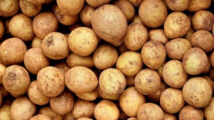 A pile of fresh sapodilla fruits neatly stacked, highlighting their earthy tones and natural surface texture in a market setting