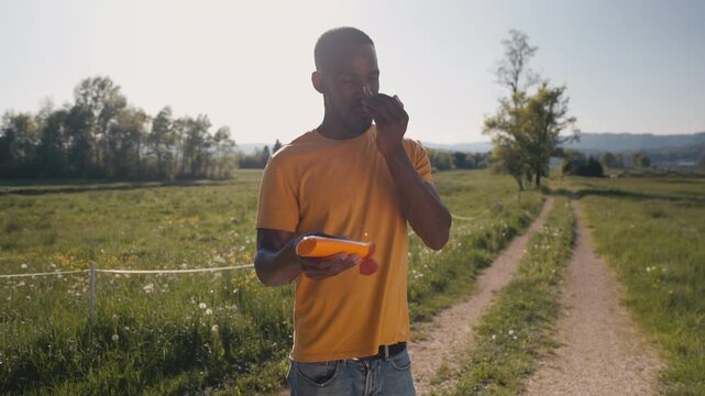 African American man preparing for a summer countryside walk, applying sunscreen to his face, gently rubbing it on his forehead, cheeks, nose, and chin, medium shot.