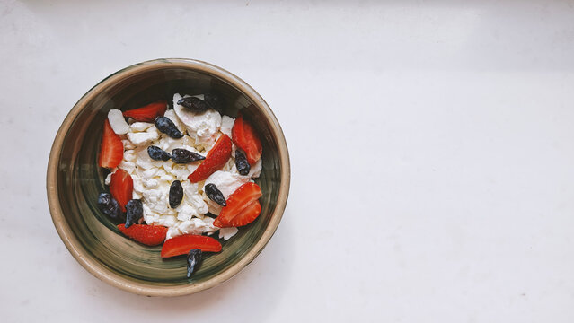 Homemade Cottage cheese with strawberries and honey berries in a ceramic bowl on the marble table, top view, copy space. Organic bio farm dairy product. Healthy eating concept.