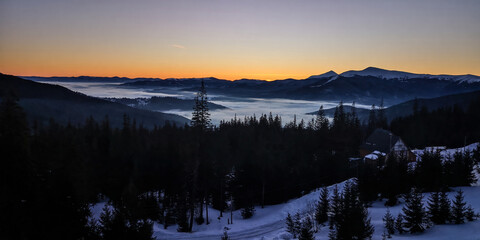 Scenic winter Carpatian mountain landscape with snowy slope panoramic view soft sunrise clouds and distant peaks in calm natural atmosphere.