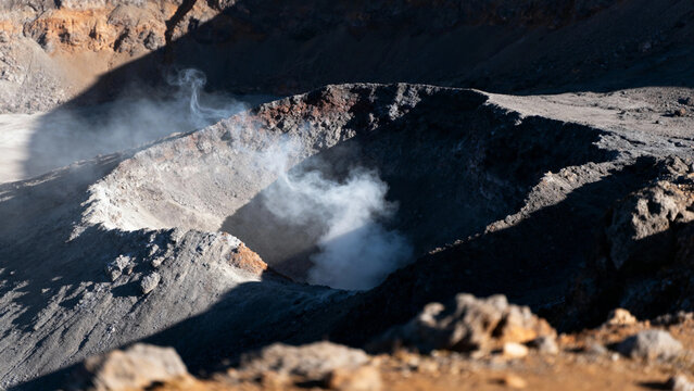 Steam rising from a volcanic crater in a rugged mountainous terrain