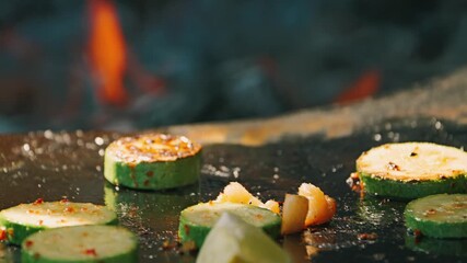 Grilled zucchini slices sizzling on a hot surface, with flames flickering in the background, creating an inviting and tantalizing cooking atmosphere
