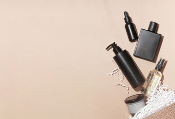 Fototapeta premium Scattered cosmetics from the beauty box, serum essence, perfume or lotion, shampoo or balm, mist or cleaning oil, clay mask or cleansing balm in black bottles on neutral beige background