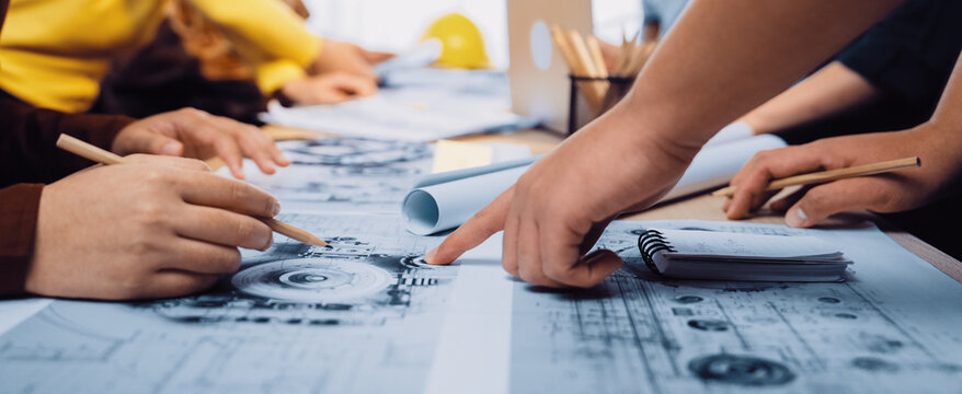 A dynamic group of design professionals engaged in a collaborative session, sketching and planning on large blueprints in a modern workspace filled with creativity. SACTR
