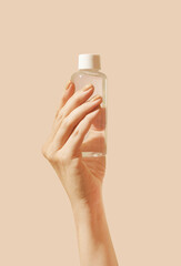Woman hand with drinking water or cosmetic product bottle: toner, cleansing water, tonic, serum, lotion or essence. Neutral beige isolated background