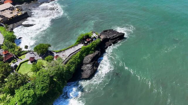 Drone video of an aerial view of the coast of Tanah Lot Temple, real time showing large rocks along the coast jutting out into the beach and white waves