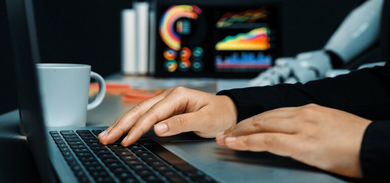 A person is typing on a laptop in a sleek office setting, with data visualizations on screen and a coffee cup nearby, showcasing a modern work atmosphere.Noogenesis