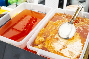 Texture of honeycombs close up. Yellow wax honeycombs with honey in plastic containers. Sale of homemade honey at the fair