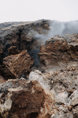 This image shows a rugged, rocky landscape with jagged earth formations and rising smoke or steam drifting through the cracks.