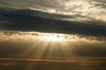 Sunset sky background, dramatic evening clouds lit by sunlight with sunny beams breaking through the clouds