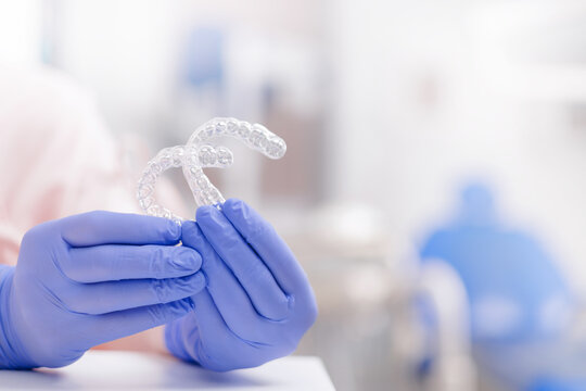 Close-up of dentists with gloves holding invisible teeth aligners in dental clinic background