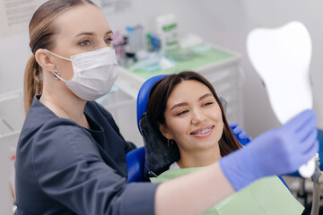 Female dentist assists asian young woman with dental checkup using mirror
