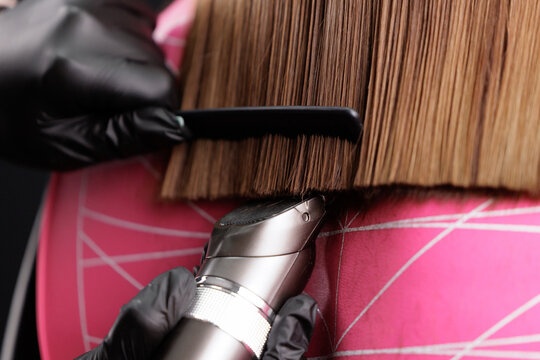 Haircut in salon, hairdresser uses comb and clippers to trim hairline of ends hair. - Powered by Adobe