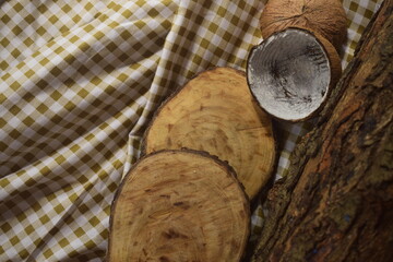 Cepos de madeira sobre tecido quadriculado marrom ao lado de tronco de árvore e coco seco ralado