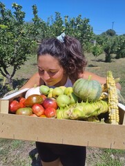 Woman holding a crate of freshly harvested organic vegetables and fruits on a sunny farm
