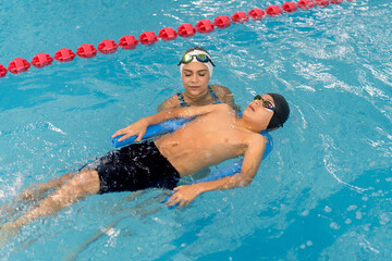 Boy learning floating technique with swimming instructor