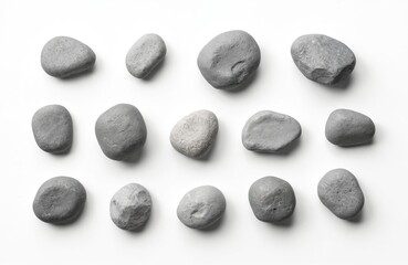 Collection of grey pebbles arranged on white surface. Smooth rounded stones offer textural contrast. Minimalist composition suggests tranquility, natural beauty. Perfect for wellness design projects.