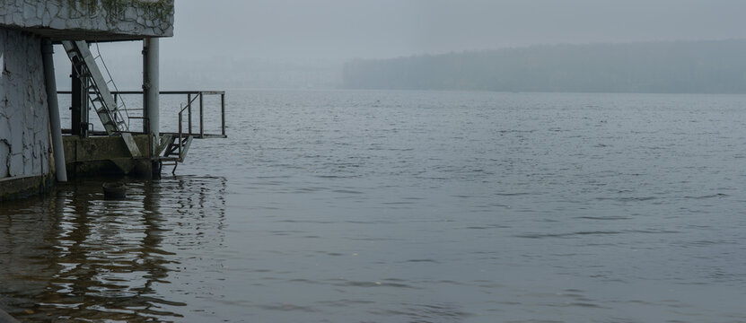 autumn lake with silhouettes of pier and opposite bank in fog in gray weather