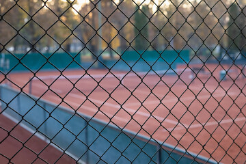 abstract tennis court view through a diamond wire mesh fence at sunset or dusk. shallow depth of field, focusing on the foreground netting