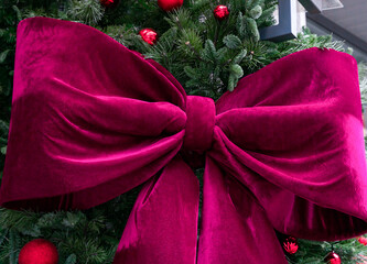 A large, luxurious magenta velvet bow displayed on a Christmas tree. The soft texture of the fabric and the festive decorations create a rich, elegant holiday atmosphere. Selective focus.