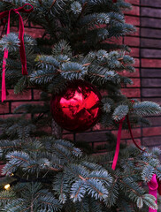 A sparkling red Christmas bauble on the green branches of a fir tree. Festive holiday decor. Selective focus.